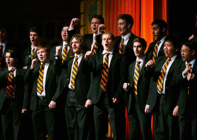 A men's choir raises their fists while singing at a OneSource Strategy alumni event