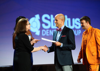 Two People Shake Hands on Stage at a OneSource Strategy Event While One Receives a Certificate
