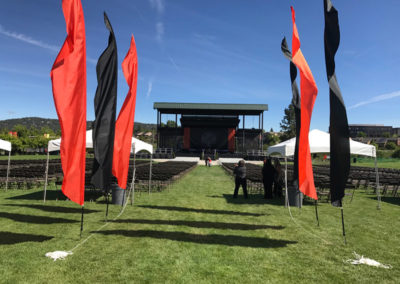 An outdoor stage with a large arrangement of chairs and vertical flags at a OneSource Strategy higher education ceremony event
