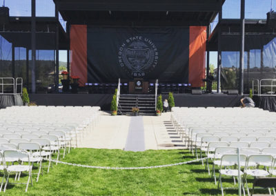 A stage in front of a lawn with a large arrangement of folding chairs at a OneSource Strategy higher education ceremony event