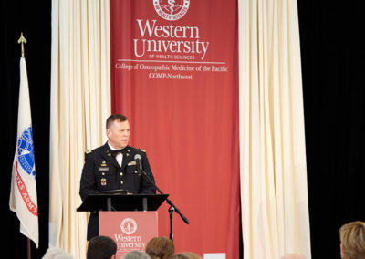 A man in military formal wear speaks at a podium at a OneSource Strategy higher education ceremony