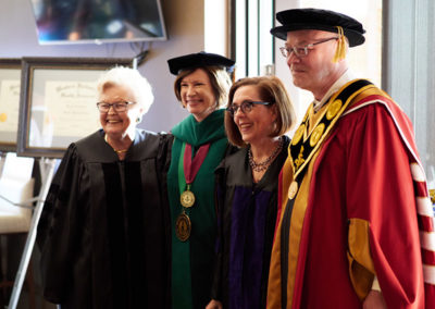 A group of people in graduation caps and gowns with governor Kate Brown at a OneSource Strategy higher education ceremony