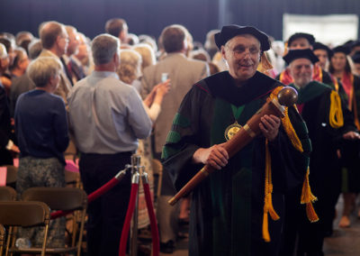 A line of people in graduation caps and gowns led by a man holding a wooden scepter at a OneSource Strategy higher education strategy