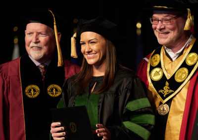 A group of three people in graduation caps and gowns at a OneSource Strategy higher education ceremony