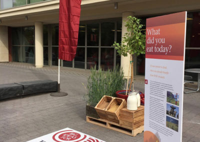 A sign asking "What did you eat today?" with additional information stands next to an arrangement of plants, grains, and jugs of milk at a OneSource Strategy higher education event