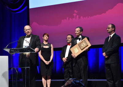 A group of five standing onstage, a man holding a cougar plaque at a OneSource Strategy higher education milestone celebration
