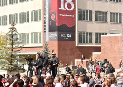 A crowd sits in folding chairs outside at a OneSource Strategy higher education milestone celebration