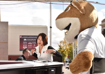A woman speaks with a cougar mascot while they sit at a counter at a OneSource Strategy higher education event