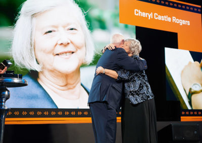 A man hugs a woman being honored onstage at a OneSource Strategy event
