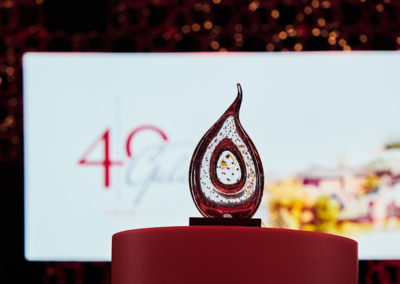 A teardrop glass trophy sits on a table in front of a large presentation screen