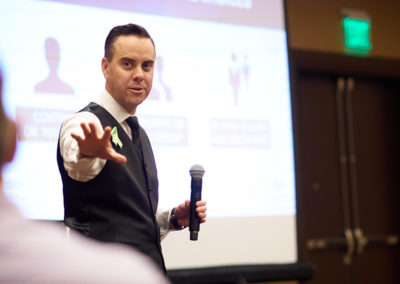 A Man Holding One Hand Outward During a Presentation at a OneSource Strategy Event